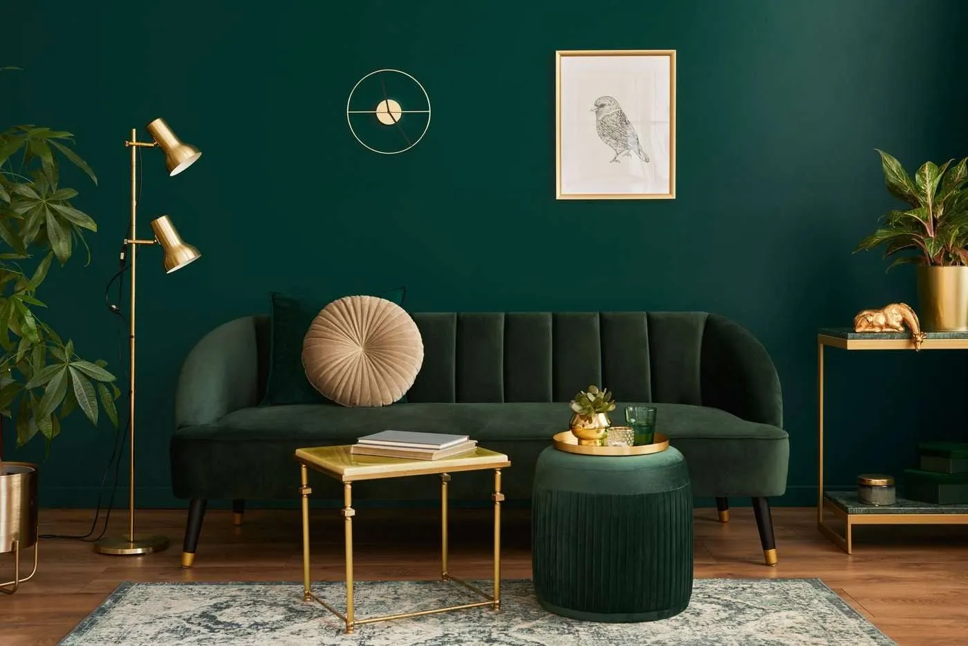 Ein gemütliches Wohnzimmer mit einem grünen Sofa und einer dunkelgrünen Wand, das mit stylischen goldenen Elementen dekoriert wurde. Ein farblich passender Teppich ergänzt das Design.