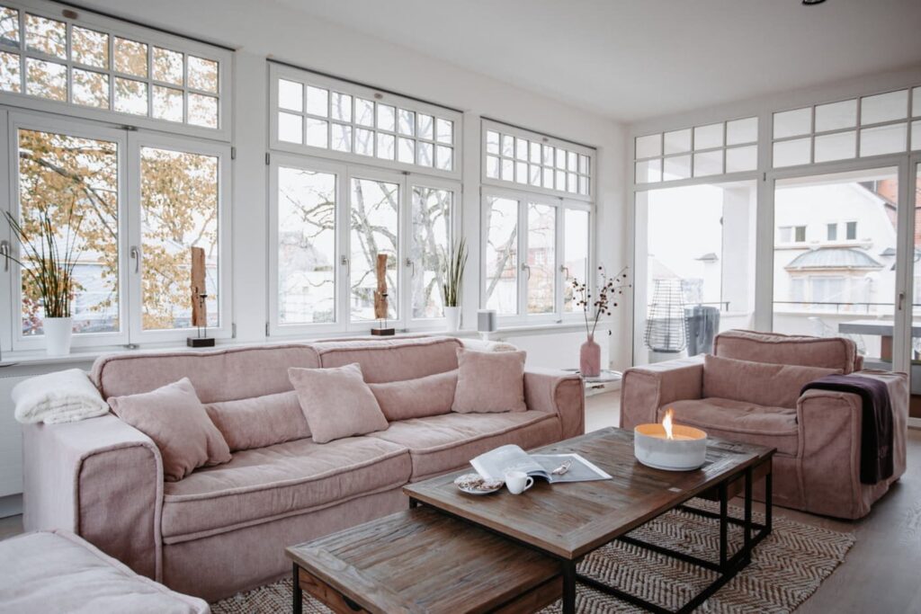 Ein Wohnzimmer mit einer großen Fensterfront vor der eine rosafarbene Couch steht